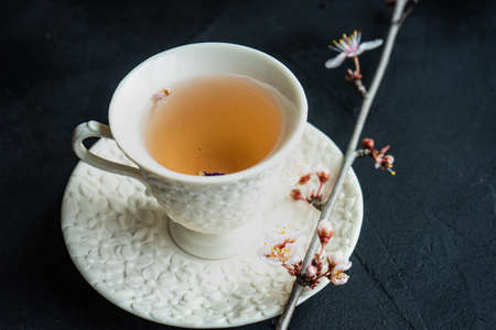 Cup of floral green tea and blooming cherry ttree branch on concrete background with copy space