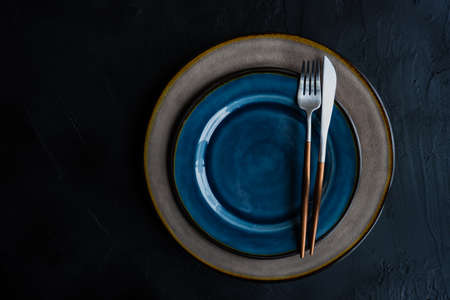 Rustic table setting with ceramic plates and modern cutlery on dark background with copy spaceの写真素材