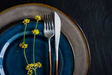 Rustic table setting with ceramic plates and modern cutlery on dark background with copy spaceの写真素材