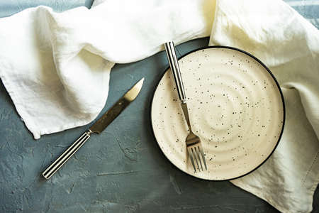 Rustic table setting with ceramic plate and modern cutlery on dark background with copy spaceの写真素材