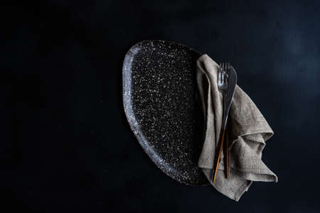Rustic table setting with ceramic plate and modern cutlery on dark background with copy spaceの写真素材