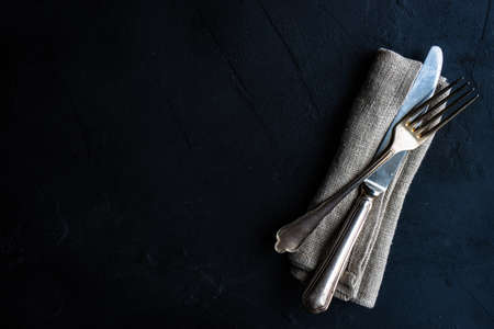 Simple vintage cutlery with napkin on stone dark background with copy space