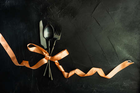 Stylish black metal cutlery with bright color ribbon on stone dark background with copy spaceの写真素材