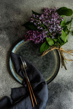 Spring table setting with beautiful lilac flowers on grey concrete background with copy space