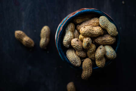 Bowl full of peanuts on dark wooden table with copy space