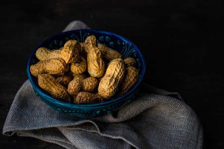 Bowl full of peanuts on dark wooden table with copy space
