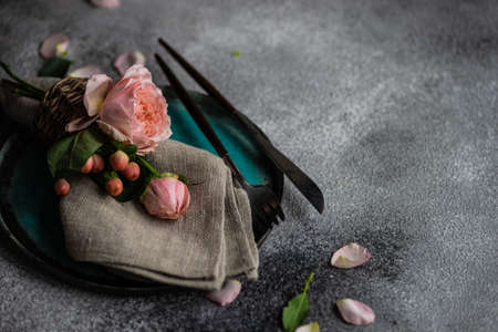Festive table setting with beautiful roses, modern plates and cutlery on rustic grey background with copy spaceの写真素材