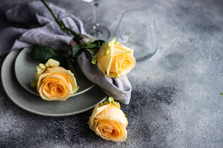 Festive table setting with beautiful roses, modern plates and cutlery on rustic grey background with...