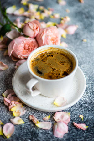 Coffee drink concept with cup of americano and roses on concrete background with copy space