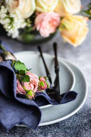 Festive table setting with beautiful roses, modern plates and cutlery on rustic grey background with...
