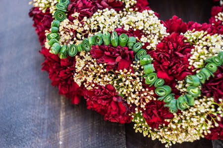 circlet of carnation flowers on dark wooden background with copyspace