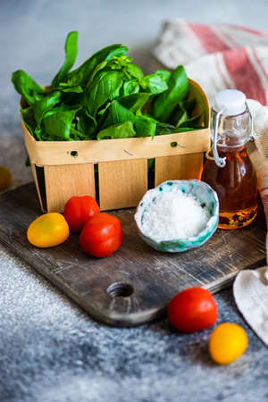Ingredients for summer vegetable salad with cherry tomatoes, basil herb, olive oil and salt on...