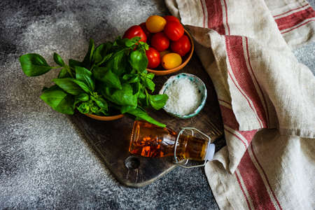 Ingredients for summer vegetable salad with cherry tomatoes, basil herb, olive oil and salt on rustic background with copy spaceの写真素材