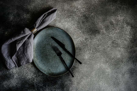 Rustic table setting with grey ceramic plates and black metal cutlery on stone grey textured background with copy spaceの写真素材