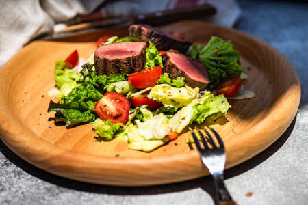 Served steak salad with beef meat and fresh organic lettuce leaves and cherry tomatoes on concrete background with copy spaceの写真素材