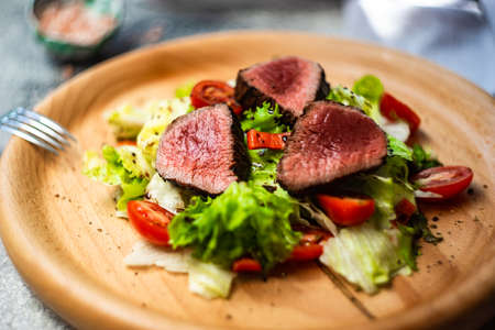 Served steak salad with beef meat and fresh organic lettuce leaves and cherry tomatoes on concrete background with copy spaceの写真素材