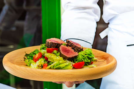 Served steak salad with beef meat and fresh organic lettuce leaves and cherry tomatoes on concrete...