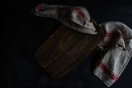 Cooking concept with vintage cutting board and rustic towel on dark stone backgroundの写真素材