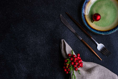 Christmas table setting concept in dark tones with red berries and fir tree