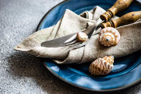 Marine cutlery set with shells and sea stars on grey concrete background with copy space
