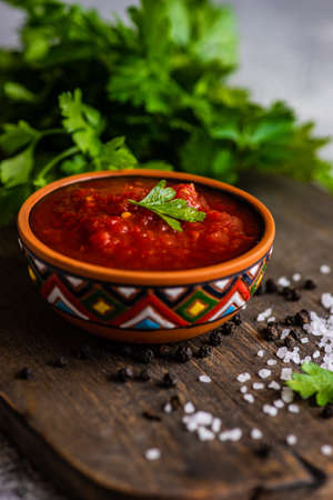 Traditional georgian tomato sauce Satsebeli in ceramic bowl with spices on rusty background with copy spaceの写真素材