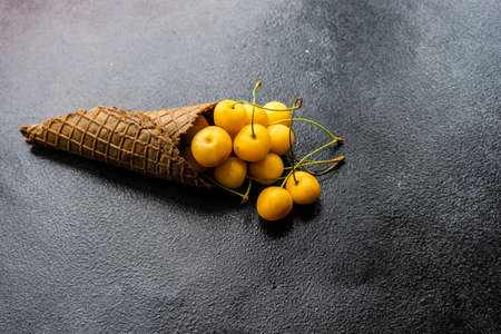 Waffle cone full of sweet cherries on dark stone background with copy space