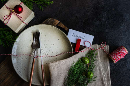 Rustic table setting for festive holiday Christmas dinner with gift box, fir tree and decor on stone...
