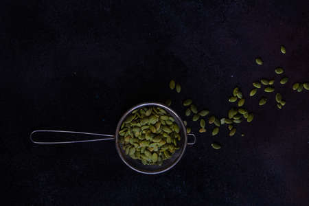 Cooking concept with strainer full of pumpkin seed on dark background with copy space