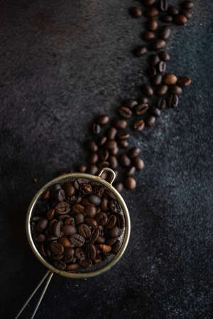 Strained full of coffee beans on dark stone background with copy space