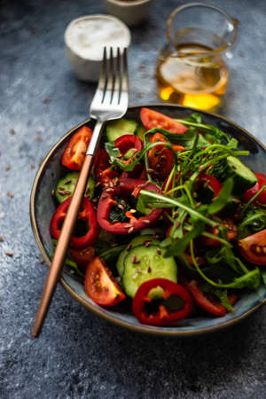 Healthy vegetable salad with organic cucumber, tomatoes, bell pepper, rocket herb and flax seeds on stone backgroundの写真素材