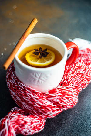 Cup of mulled tea with spices and lemon with red and white knitted scarf on stone background with...