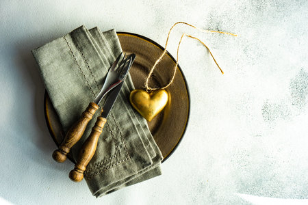 Rustic table setting with ceramic plate and vintage cutlery decorated with golden heart on stone background with copy spaceの写真素材