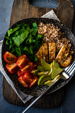 Healthy breakfast concept with bowl full of buckwheat, avocado, tomatoes, spinach and meat on concrete background with copy spaceの写真素材