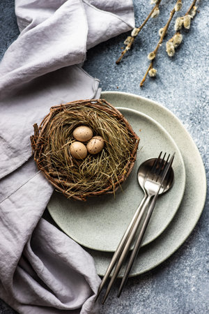 Festive holiday table setting for Easter dinner decorated with colored eggs on stone background with...
