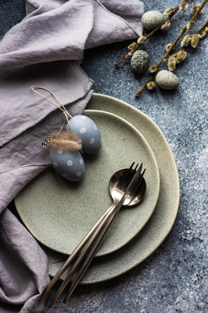 Festive holiday table setting for Easter dinner decorated with colored eggs on stone background with...