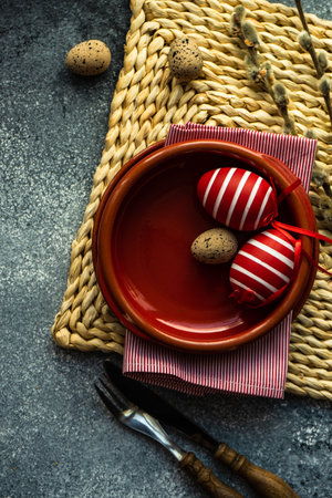 Festive holiday table setting for Easter dinner decorated with colored eggs on stone background with...