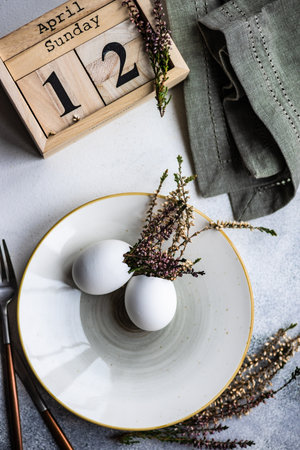 Festive table setting for holiday Easter dinner decorated with eggs and heather flowers on stone...