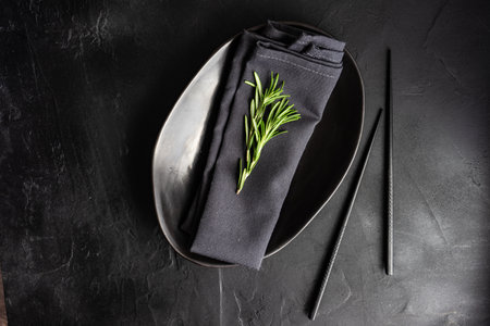 Minimalistic table setting with textured ceramic plate and chopsticks on concrete background with copy space in black colorの写真素材