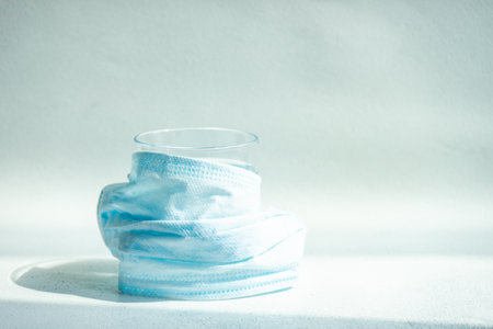 COVID-19 virus concept with glass of water and  face mask on pastel background with copy space