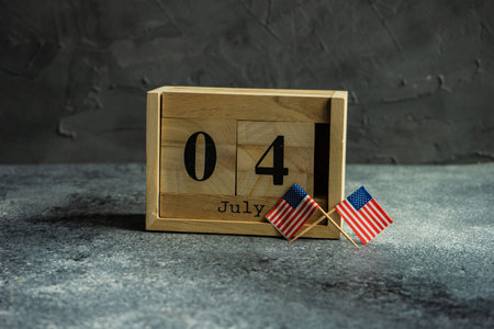 4th July celebration card concept with wooden calendar and USA flags on grey background with copy...