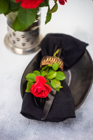 Table setting with fresh red rose flower and black plate and cutlery on stone background with copy spaceの写真素材