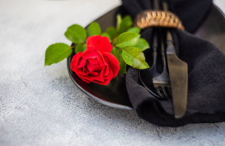 Table setting with fresh red rose flower and black plate and cutlery on stone background with copy spaceの写真素材