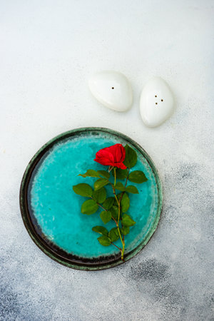 Table setting with fresh red rose flower on mint green ceramic plate on stone background with copy spaceの写真素材