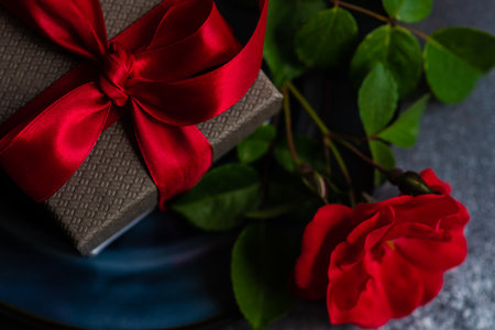 Table setting with fresh red rose flower on dark blue plate with gift box on stone background with copy spaceの写真素材