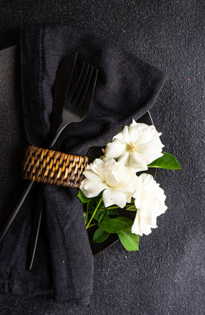 Minimalistic table setting with black stoneware and cutlery decorated with white rose flower on black stone table with copy spaceの写真素材