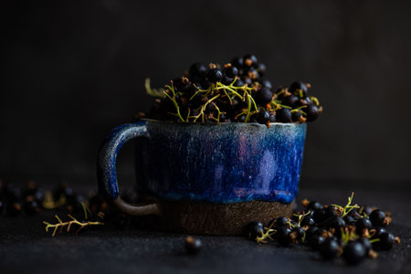 Fresh organic black currant berries in a ceramic bowl on dark background with copy space