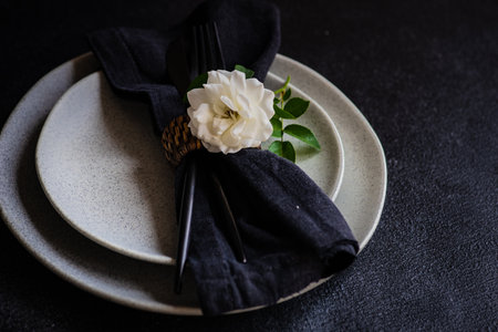 Minimalistic table setting with modern stoneware and cutlery decorated with white rose flower on...