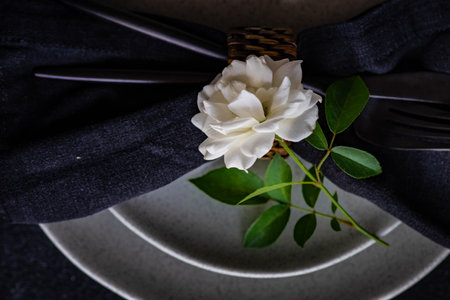 Minimalistic table setting with modern stoneware and cutlery decorated with white rose flower on black stone table with copy spaceの写真素材