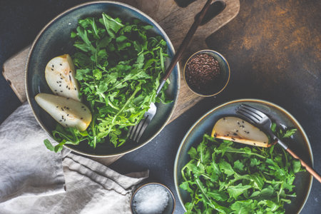 Organic food concept with fresh raw rucola leaves and pear slices with sesame seeds and olive oil on concrete background with copy spaceの写真素材