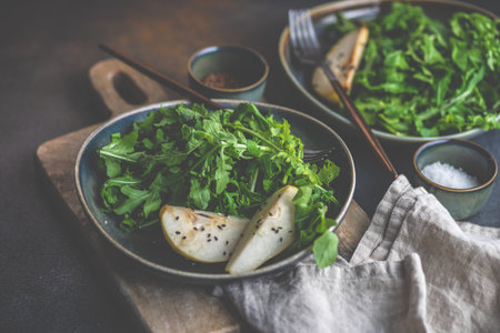 Organic food concept with fresh raw rucola leaves and pear slices with sesame seeds and olive oil on...
